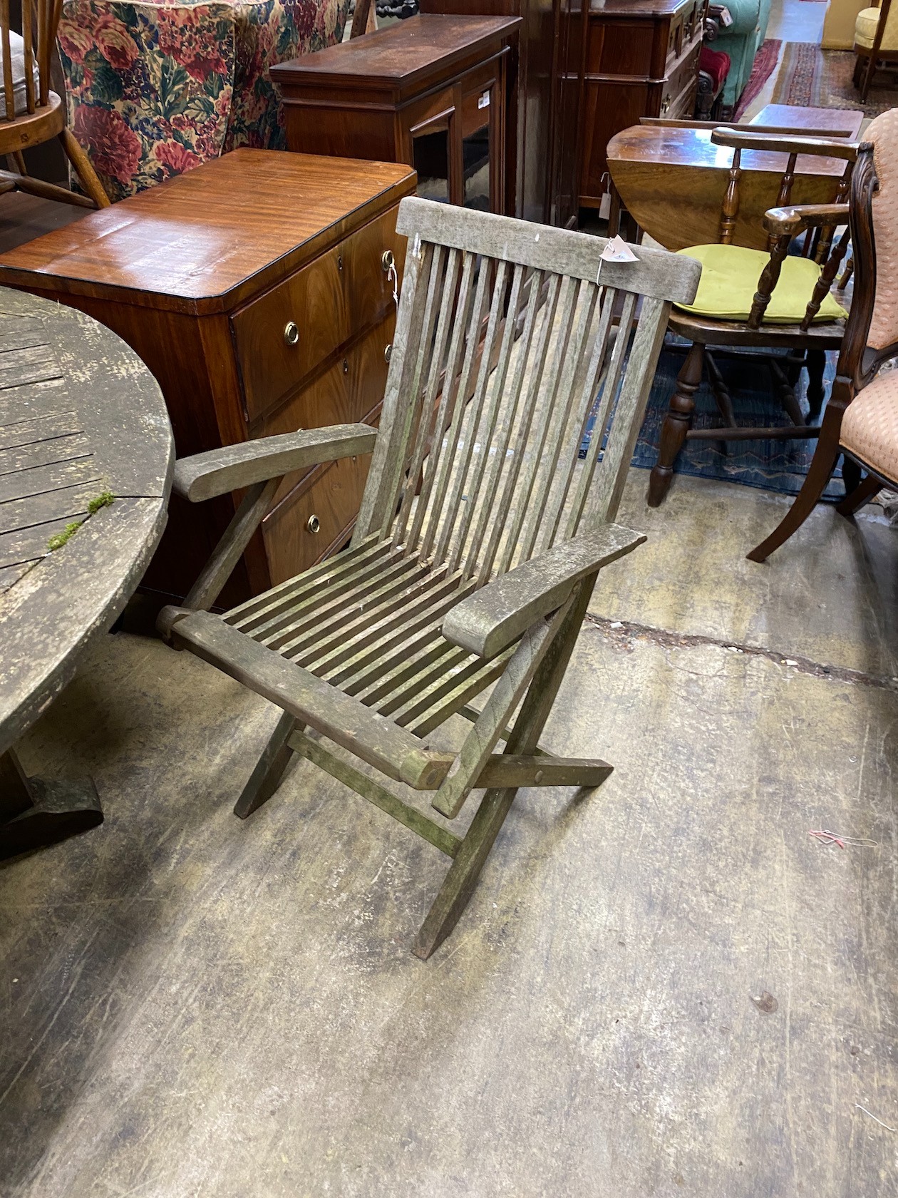 A weathered teak circular garden table, diameter 150cm, height 75cm, a matched set of six folding teak garden elbow chairs, two with arms and a teak garden bench